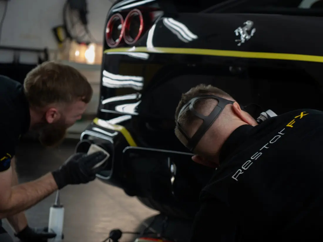 Deux techniciens RestorFX restaurent la carrosserie noire d'une Ferrari dans un centre